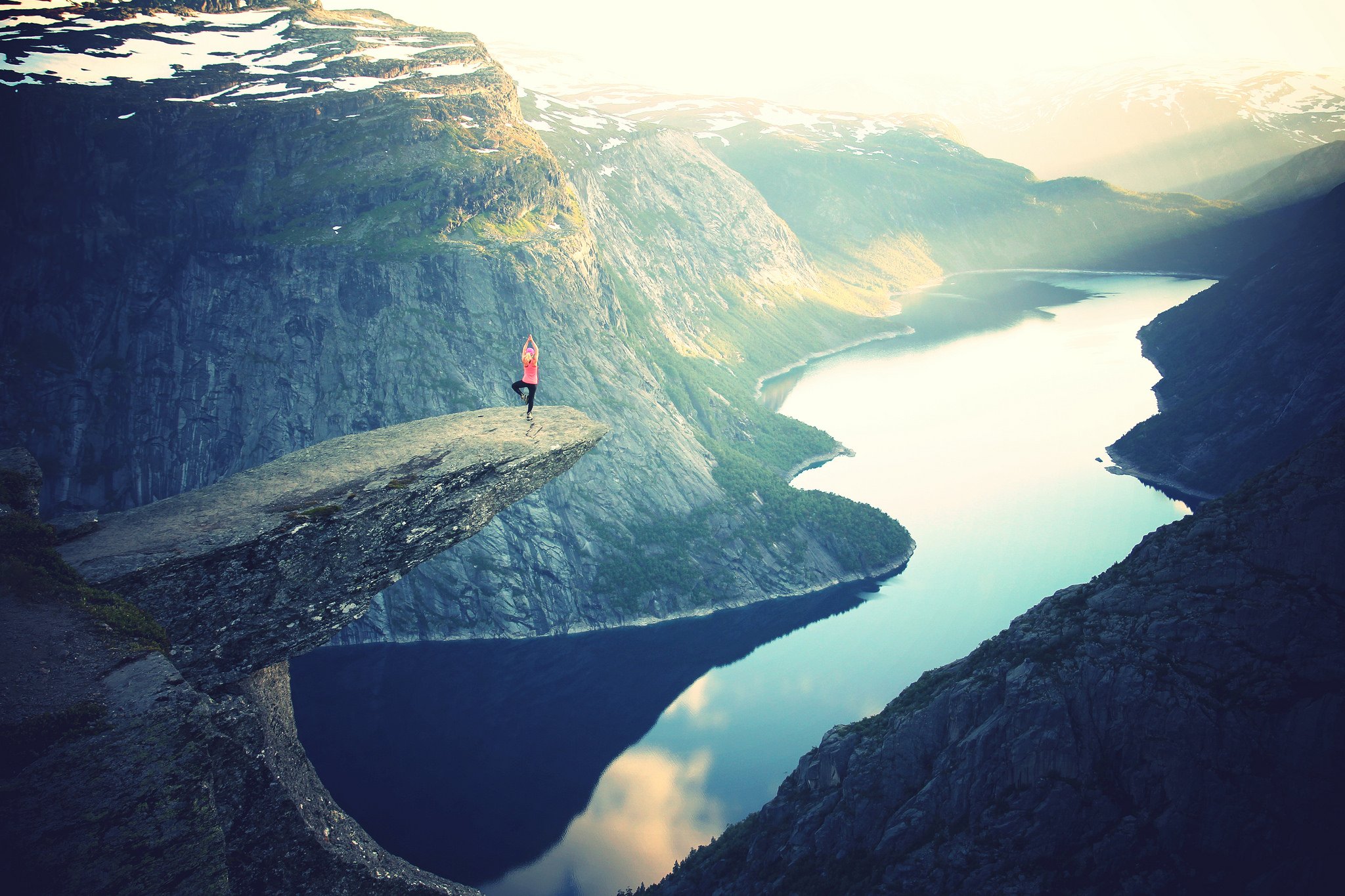 person doing yoga on a cliff edge with mountain and river in background